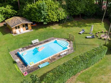 An outdoor swimming pool with floaties and benches in a garden with lawn chairs a wooden shed and a fire pit area at Deer Leap House in Moreton