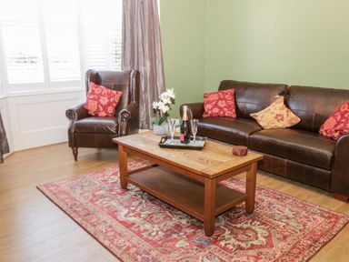 A sitting room with a brown leather sofa and armchair with red and beige cushions a wooden coffee table with a bottle and two glasses on a red patterned rug at Hazeldene in Sleights