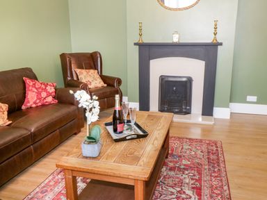 A living room with a brown sofa and armchair a wooden coffee table a fireplace and a red patterned rug at Hazeldene in Sleights