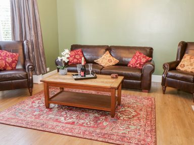 A living room with brown leather sofa and chairs red and beige cushions wooden coffee table with tray and bottle on a red patterned rug at Hazeldene in Sleights