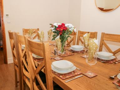 A dining table with wooden chairs set with plates glasses and napkins and a vase with red and white flowers at Hazeldene in Sleights