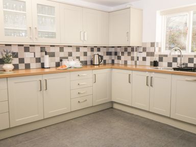 A kitchen with cream cabinets wooden countertops checkered tile backsplash and a window at Hazeldene in Sleights