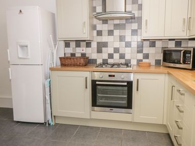 A kitchen with a freezer fridge ironing board gas stove oven microwave and tiled backsplash at Hazeldene in Sleights