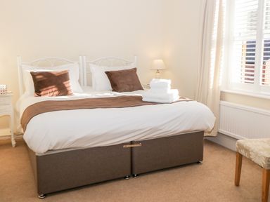 A bedroom with a double bed with brown cushions white bed linen folded towels bedside table with lamp and window with blinds at Hazeldene in Sleights