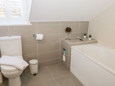 A bathroom with a toilet a towel a trash bin a bathtub a small shelf with a mirror and two small potted plants at Hazeldene in Sleights