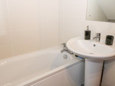 A bathroom with a white bathtub and a white sink with black soap dispenser and tumbler at Hazeldene in Sleights
