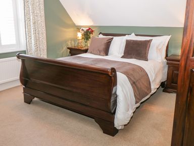 A bedroom with a wooden bed with white and brown bedding bedside tables with lamps and flowers at Hazeldene in Sleights