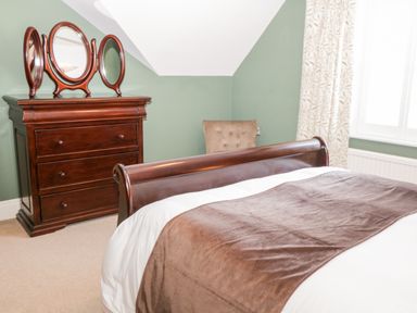 A bedroom with a wooden dresser and a tri-fold mirror next to a bed with a brown blanket at Hazeldene in Sleights