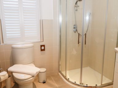 A bathroom with a toilet a towel on the toilet seat a small bin a shower with glass doors and a window with shutters at Hazeldene in Sleights