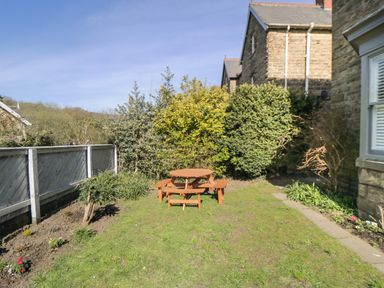 A garden with a wooden picnic table surrounded by shrubs and a stone house at Hazeldene in Sleights