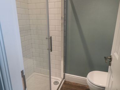 A bathroom with a glass shower enclosure tiled with white subway tiles and a white toilet at Hazeldene in Sleights