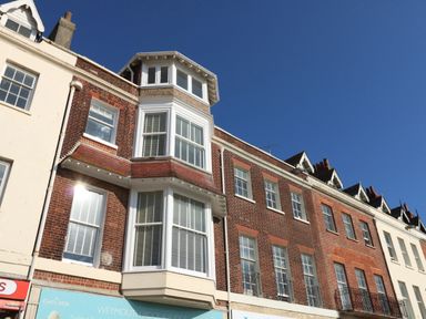 A row of red brick and white buildings with multiple windows under a clear blue sky at The Kings Statue in Weymouth