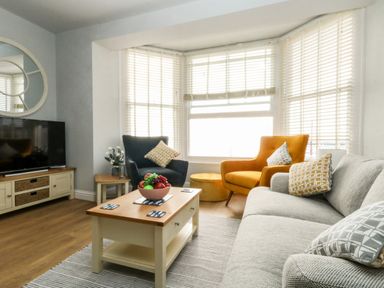 A living room with a gray sofa, orange and blue armchairs, wooden coffee table with fruit bowl and TV at The Kings Statue in Weymouth