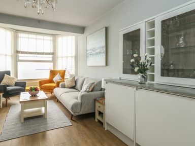 A living room with a gray sofa, yellow and gray armchairs, coffee table with fruit bowl, and white cabinet with flowers at The Kings Statue in Weymouth