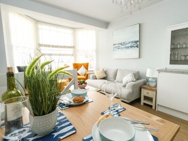 A dining table set with bowls plates and glasses with a living room in the background at The Kings Statue in Weymouth