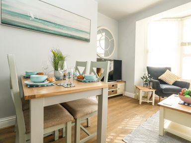 A dining table with chairs set with bowls and glasses next to a living area with an armchair and coffee table at The Kings Statue in Weymouth