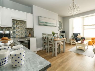 A kitchen and dining area with a table set for four and a living space with chairs and a coffee table at The Kings Statue in Weymouth