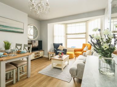 A living room with a grey sofa orange and dark blue armchairs a coffee table dining table with chairs and a TV at The Kings Statue in Weymouth
