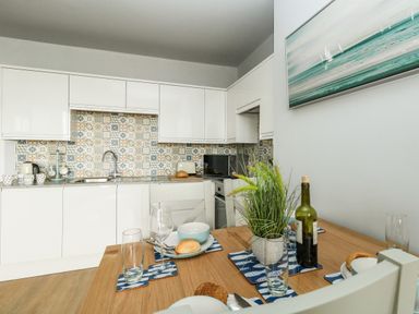 A kitchen with white cabinets and patterned tile backsplash with a dining table set with plates glasses and a plant at The Kings Statue in Weymouth
