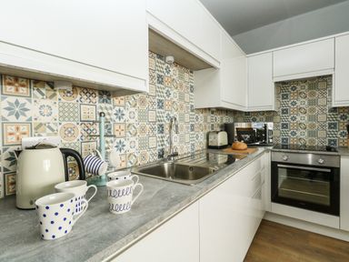 A kitchen with white cabinets a patterned tile backsplash a sink kettle mugs toaster microwave and oven at The Kings Statue in Weymouth