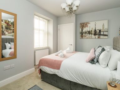 A bedroom with a double bed cushions a wall painting and a window with blinds at The Kings Statue in Weymouth