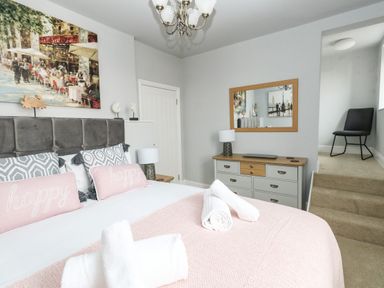 A bedroom with a bed with pink pillows and towels on it a dresser with a lamp and mirror and a chair up a short flight of stairs at The Kings Statue in Weymouth