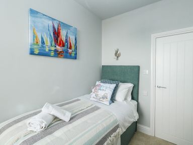 A bedroom with a single bed a striped blanket and a painting of sailboats at The Kings Statue in Weymouth