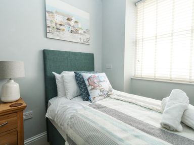 A bedroom with a single bed a bedside table with a lamp and a window with blinds at The Kings Statue in Weymouth