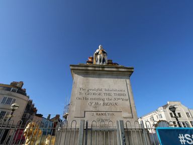 A statue of George the Third on a stone pedestal in a town square at The Kings Statue in Weymouth