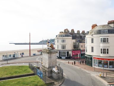 A seaside street with a statue and round buildings near the beach at The Kings Statue in Weymouth