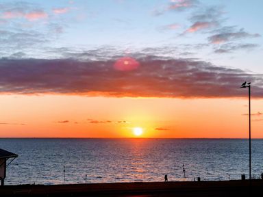 A sunset over the sea with a cloudy sky and two people walking along the shore at Maples in Hunstanton