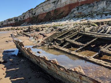 A beach with the remains of a wooden shipwreck and cliffs in the background at Maples in Hunstanton