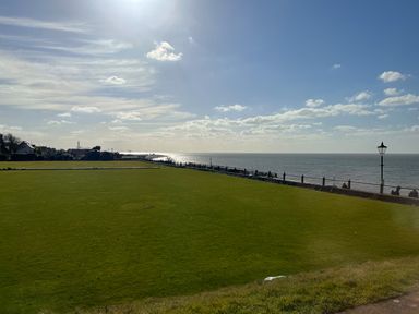 A large grass field next to a seaside promenade with people sitting on benches and houses in the background at Maples in Hunstanton