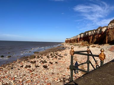 A rocky beach with cliffs in the background and people walking near the shore at Maples in Hunstanton