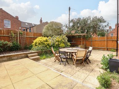 A fenced backyard with a round table and six chairs on stone paving at Maples in Hunstanton