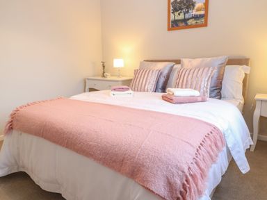 A bedroom with a bed featuring white sheets and a pink blanket with pillows and folded towels on top at The Seventeen in Bourton-On-The-Water