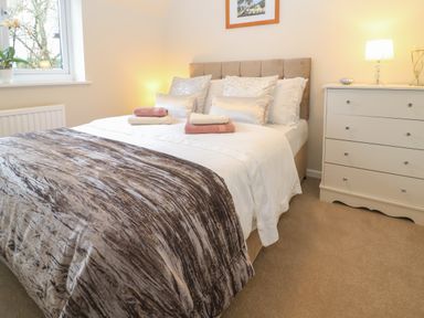 A bedroom with a bed with pillows and folded towels next to a white dresser and window at The Seventeen in Bourton-On-The-Water