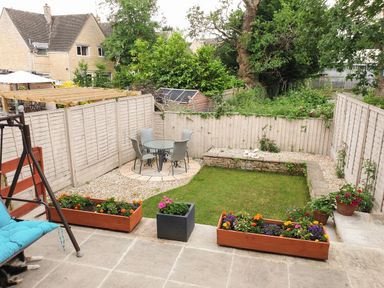 A small backyard garden with a lawn glass table with four chairs flower pots and wooden fences at The Seventeen in Bourton-On-The-Water
