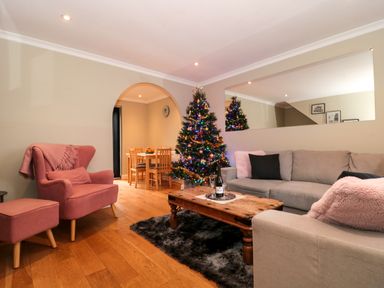 A living room with a Christmas tree and pink armchair near a wooden coffee table at The Seventeen in Bourton-On-The-Water