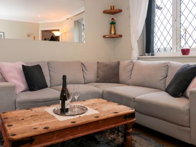 A living room with a grey sectional sofa and wooden coffee table with a bottle and glasses at The Seventeen in Bourton-On-The-Water