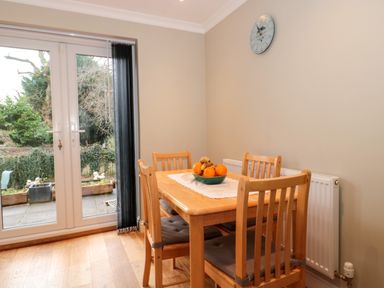 A dining area with a wooden table and four chairs and a bowl of fruit on the table near glass doors at The Seventeen in Bourton-On-The-Water