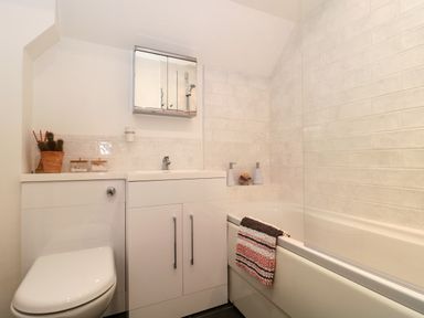A bathroom with a toilet sink with storage cabinet above and a bathtub with tiled walls at The Seventeen in Bourton-On-The-Water
