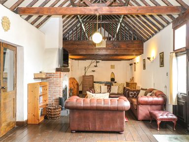 A living room with exposed wooden beams leather sofas a fireplace and a wooden floor at The Old Barn in Walcott