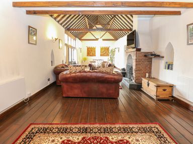 A living room with brown leather sofas a fireplace wooden beams and a patterned rug at The Old Barn in Walcott