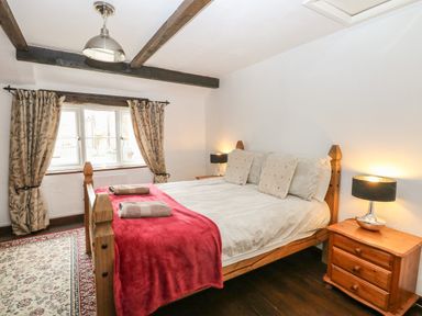 A bedroom with a wooden bed with pillows and blankets two bedside tables with lamps and a window with curtains at The Old Barn in Walcott