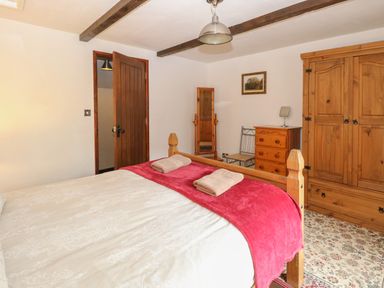 A bedroom with a wooden bed with towels on a red blanket a wooden wardrobe chest of drawers and a full-length mirror at The Old Barn in Walcott