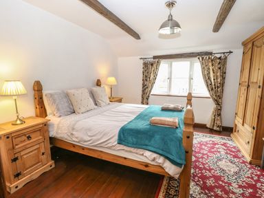 A bedroom with a wooden bed frame two bedside tables with lamps a wardrobe and a patterned rug at The Old Barn in Walcott