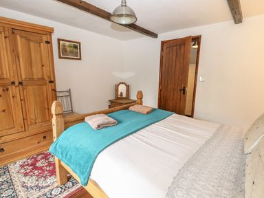 A bedroom with a wooden bed with a blue blanket and two towels a wooden wardrobe a bedside table with mirror and a wooden door at The Old Barn in Walcott