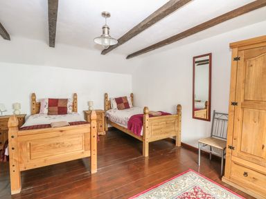 A bedroom with two wooden beds bedside tables wardrobe mirror and a chair at The Old Barn in Walcott