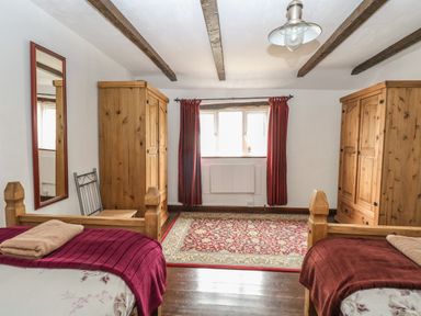 A bedroom with two wooden beds red blankets two wooden wardrobes a patterned rug and red curtains at The Old Barn in Walcott